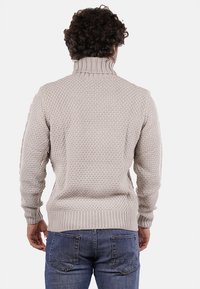Maglione lavorato a maglia in beige chiaro, con colletto alto, motivo testurizzato e polsini e orlo a costine. Indossato con jeans blu.