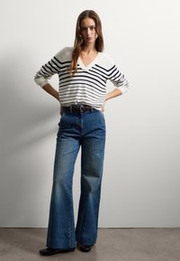 Suéter de pico a rayas en blanco y marino, combinado con jeans de pierna ancha de mezclilla azul de tiro alto. Incluye cinturón marrón y botas negras hasta el tobillo.