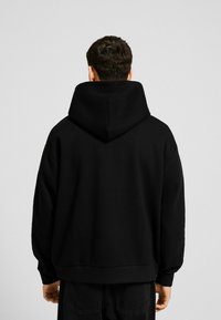 Svart oversized hoodie med en stor huva, sänkt axlar och ribbade ärmslut. Tillverkad av mjukt tyg med en slät yta.