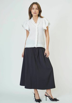 White short-sleeve blouse with textured fabric and lace detailing, paired with a long black pleated skirt and black high-heeled shoes.