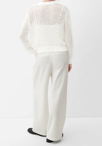 Vit, stickad tröja med en strukturerad öppen väv och ribbat nederkant, kombinerad med krämfärgade vida byxor och svarta platta skor.