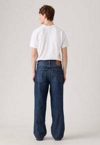 Blauwe denim jeans met een hoge taille en een wijde pijp, met een leren logo-label op de achterkant. De stof heeft een klassieke textuur en afwerking.