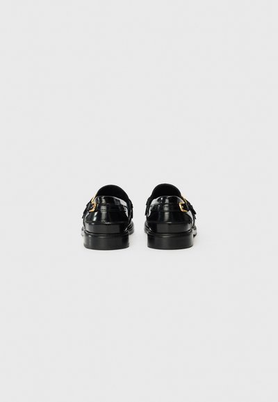 Zapatos de charol negros con un diseño elegante. Tienen un tacón bajo, un talón abierto y detalles en dorado en las correas.