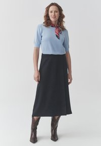Maglione azzurro chiaro a maniche corte, gonna nera lunga fino al ginocchio e stivali da cowboy marroni. Sciarpa con motivo rosso e nero annodata al collo.