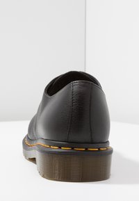 Scarpa in pelle nera con tacco arrotondato e suola in gomma testurizzata. Presenta una cucitura arancione a contrasto lungo il bordo della suola.