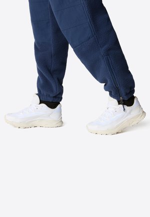 Hvite sportsko med strukturert mesh og gummisåler, kombinert med marineblå fleece-joggebukser med innsvingt design og glidelåsdetaljer.