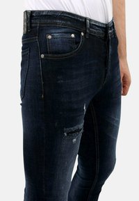 Donkerdenim jeans met een slim fit, voorzien van versleten accenten op de bovenbenen en blauwe stiksels, vijf zakken en details van zilverhardware.