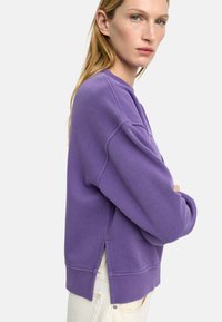Fioletowa bluza z luźnym krojem, ściągaczami przy rękawach oraz rozcięciem po bokach u dołu. Wykonana z miękkiej bawełnianej dzianiny.