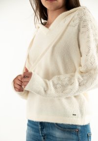 Felpa bianca, morbida, a maglia con scollatura a V e maniche a motivo testurizzato. Presenta una tasca frontale e polsini a costine, abbinata a jeans blu.