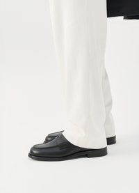 Mustad nahast loafers, millel on õmmeldud muster, koos heledate kohandatud pükstega, näidates sujuvat ja läikivat pinda.