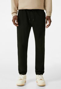 Pantalon de jogging noir en tissu doux, avec une taille élastique à cordon, des chevilles resserrées et des poches latérales.