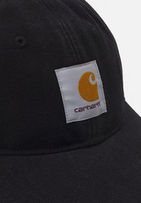 Gorra de béisbol de algodón negra con un parche rectangular blanco y naranja que presenta el texto "carhartt". Textura suave, forma redonda.
