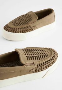 Lysbrune slip-on sko med vævet tekstur på overdelen, hvid gummisål og subtile syninger. Flad design og rund form.