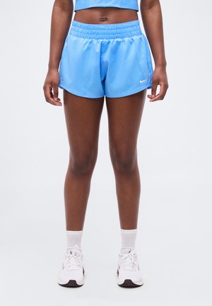 Personne debout portant un short de sport bleu clair, des chaussettes blanches et des chaussures de course blanches sur un fond uni.