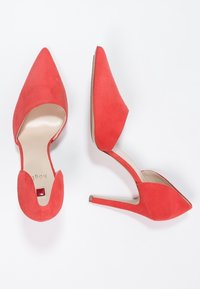 Chaussures à talons hauts en daim rouge avec un bout pointu, une ouverture à l'arrière et une silhouette légèrement courbée. Présente un accent subtil au niveau du talon.