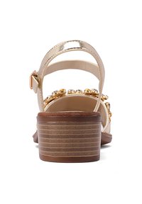 Sandal con tacco dorato metallico e cinturino, con una soletta beige liscia, adornato con perline decorative e un design con effetto legno texturizzato sul tacco.