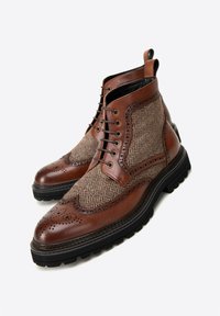 Hnědé kožené kotníkové boty s panely z herringbone látky, brogue detaily, černou gumovou podrážkou a šněrováním vpředu.