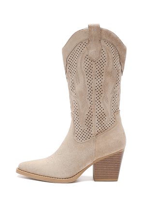 Beige Wildleder-Cowboystiefel mit spitzer Zehenpartie, dekorativen Ausschnitten und gestapeltem Absatz. Eingerahmtes Texturmuster am Schaft und glatte Sohle.