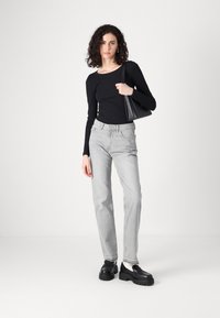 Svart ribbet langermet topp parret med lys grå rette jeans og kraftige svarte loafers. Modellen holder en liten svart håndveske.