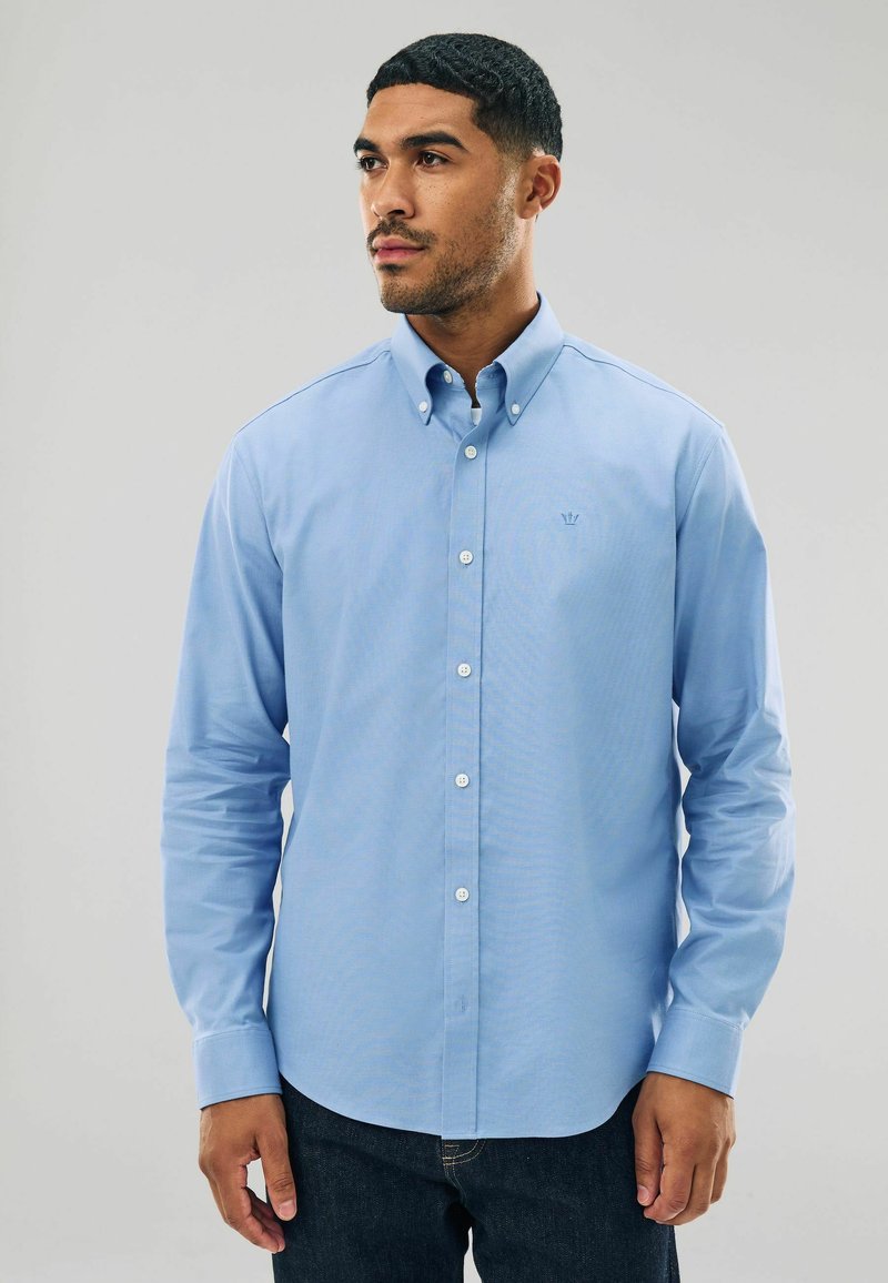 Šviesiai mėlyna marškinėlių palaidinė su apykakle, ilgomis rankovėmis ir pritaikytu siluetu. Yra mažas, siuvinėtas logotipas ant krūtinės. Pagaminta iš medvilnės.