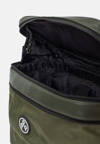 Intérieur d'un sac à dos en nylon vert avec doublure en tissu noir ; doté d'une fermeture éclair et d'une poche élastique. Étiquette de logo visible.