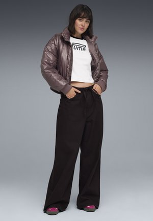 Giacca bomber imbottita di colore viola con colletto alto, t-shirt corta bianca con logo "PUMA", e pantaloni neri larghi con vita regolabile.