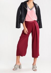 Giacca da biker in pelle nera, top senza maniche rosa con scollatura di perline, culotte color bordeaux e sandali con tacco a righe bianche e nere.