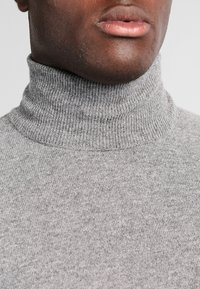 Maglione grigio a collo alto con una texture a costine, caratterizzato da un colletto aderente e un tessuto morbido, adatto per essere indossato a strati o per il tempo libero.