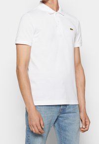 Polo blanc en coton, doté d'un col classique, de manches courtes et d'un petit logo crocodile vert sur la poitrine.