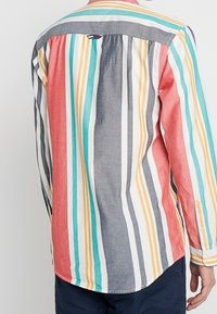 Camicia a righe con motivi verticali in corallo, grigio, blu e giallo. Realizzata in tessuto leggero con colletto e polsini bottonati.