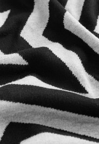 Tissu tricoté présentant un motif en zigzag noir et blanc, mettant en avant une texture douce avec une finition lisse et des épaisseurs variées.