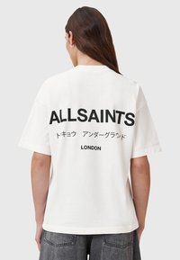 Biała bawełniana koszulka z odważnym czarnym napisem: "ALLSAINTS", japońskimi znakami oraz napisem "LONDYN" na plecach. Luźny krój, krótkie rękawy.