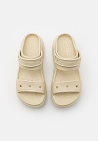Paire de sandales Crocs beige avec brides de talon réglables et trous de ventilation sur fond blanc.