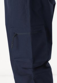 Navy cargo pants feature a zipper pocket on the side, made of smooth fabric with a subtle sheen, designed for functionality and durability.