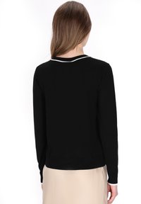 Maglione nero a maglia con maniche lunghe, rifiniture bianche nel collo e una silhouette aderente. Texture liscia e design semplice senza motivi.