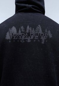 Felpa nera con cappuccio realizzata in tessuto testurizzato e una leggera grafica grigia di alberi con il testo "NAPAPIJRI geographi" sottostante.