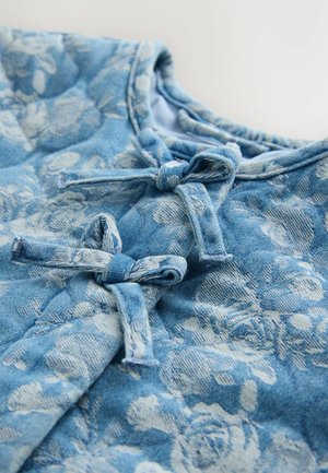 Ljusblå denimtopp med blommönster. Har tre tygrosetter vid halsringningen och en mjuk, strukturerad finish med rundad krage.