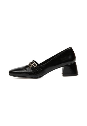 Zapato de charol negro con punta afilada, presenta acentos de doble hebilla y un tacón de bloque para mayor estabilidad. Textura suave y diseño elegante.