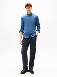 Modra teksturirana sweatshirt, nanesena čez denimsko srajco, v kombinaciji s temnimi, ohlapnimi hlačami in črnimi čevlji. Gladka tekstilna obdelava.