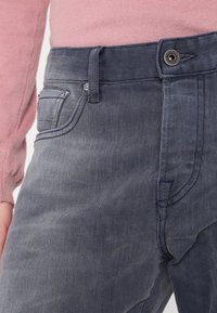 Los vaqueros de mezclilla azul oscuro presentan un diseño clásico de cinco bolsillos, cierre de botón y un ligero desvanecimiento a lo largo de los muslos. Tejido texturizado con un ligero estiramiento.