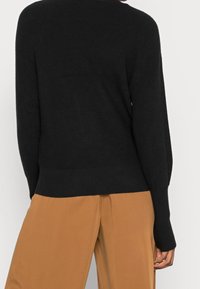 Zwart gebreide trui met wijde mouwen en een relaxed fit, met ribbelboorden en onderrand, gecombineerd met beige wijde broek.