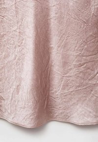 Tessuto rosa pallido con una texture increspata, morbida lucentezza e un bordo liscio. Il materiale appare leggero e si drappeggia delicatamente.