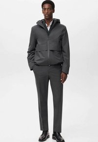 Giacca grigia con zip e cappuccio, caratterizzata da un design corto e due tasche frontali; abbinata a pantaloni tagliati coordinati e scarpe nere.