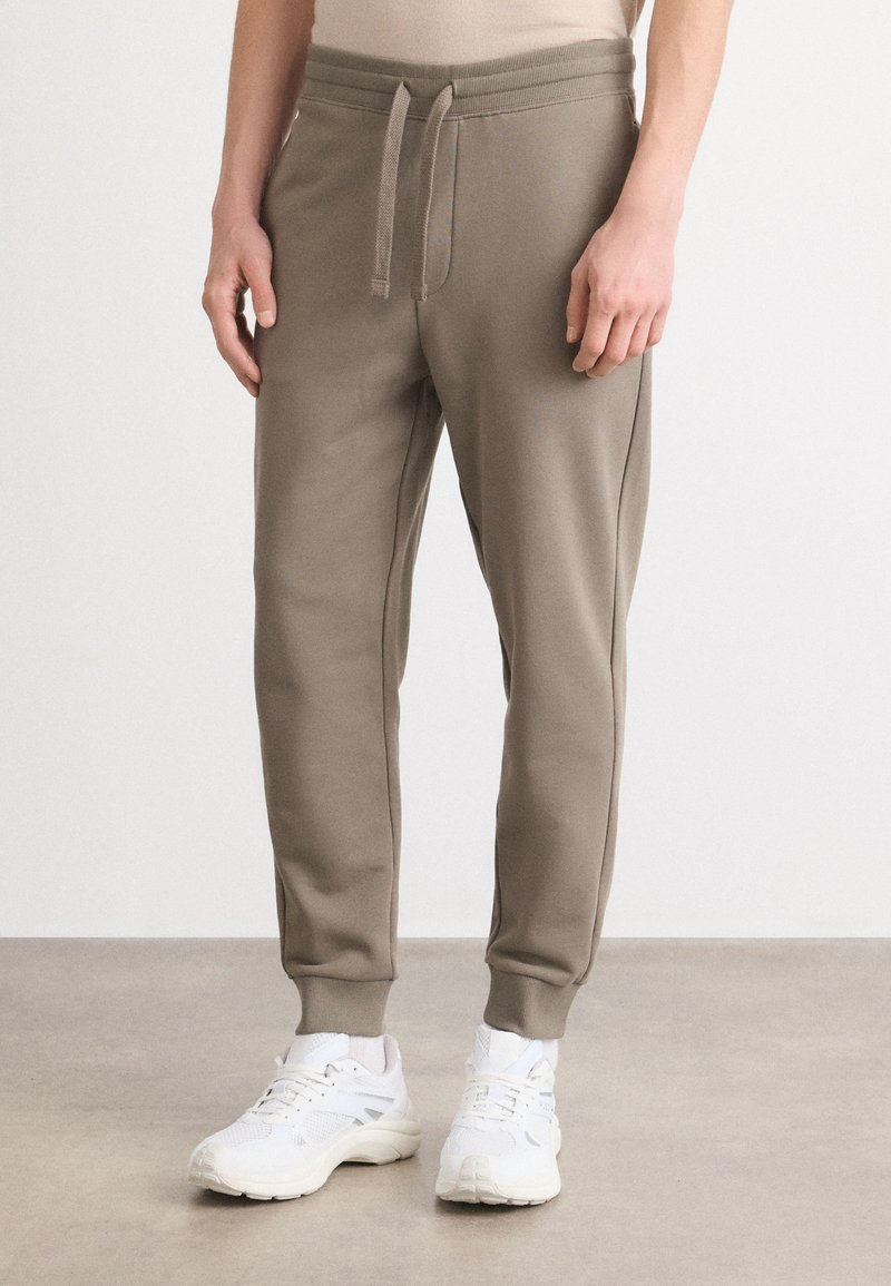 Jemné jogger nohavice z bavlnenej zmesi v tlmenej taupe farbe, s elastickým pásom a manžetami, bočnými vreckami a uvoľneným strihom.