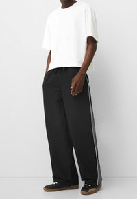 Lösa svarta byxor med vita sidostråk, tillsammans med en kortärmad vit T-shirt. Elastisk midja med justerbar dragsko.