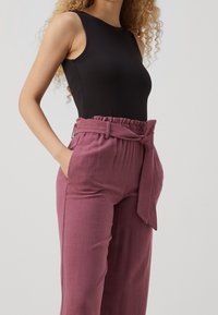 Body noir sans manches associé à un pantalon bordeaux taille haute, plissé, à texture douce, doté d'une ceinture nouée et de poches latérales.