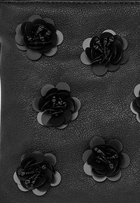 Black textured leather surface adorned with evenly spaced black layered flower appliques with coiled bead centers.