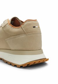 Sneaker in suede beige con lato traforato, suola intermedia bianca, suola esterna marrone e piccolo dettaglio ricamato nero, bianco e tannino sul tallone.