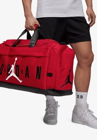 Piros sporttáska fekete részletekkel, nagy "JORDAN" grafikával és Jumpman logóval. Vastag pántokkal és tartós anyagból készült szerkezettel.