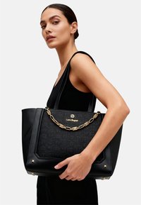 Borsa tote nera con design testurizzato, dettaglio in catena dorata, manici grandi e logo. Presenta una forma strutturata e dettagli hardware sottili.